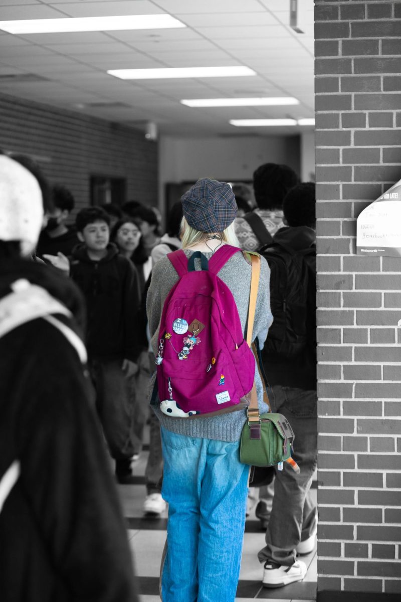 Finn Boggs walks through a crowded hallways during transition. Their backpack is covered in pins showing support for the LGBTQ+ community.