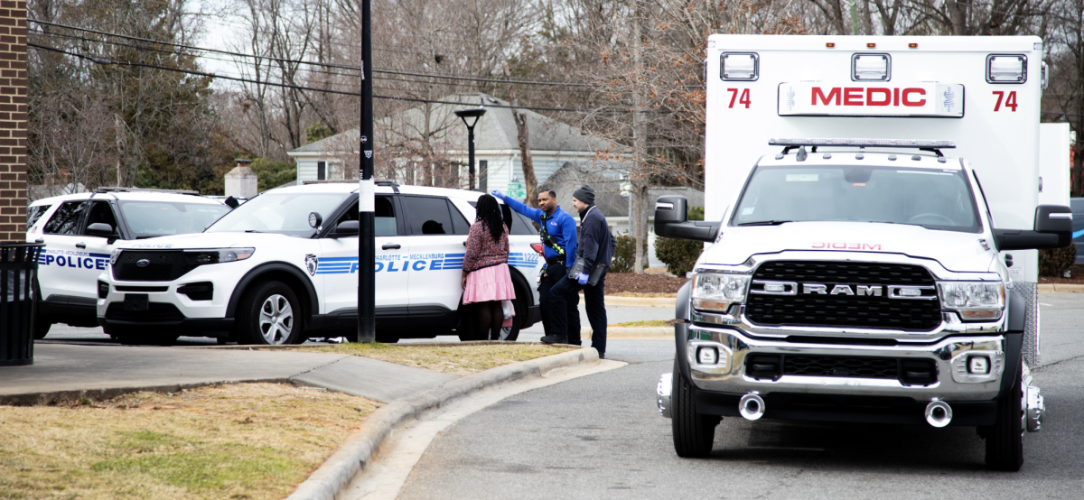 Police officers and medics gather around a woman in the Wingstop parking lot across from East Meck right before school dismissal.